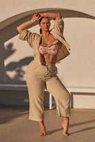 blonde model wearing a sand coloured mid calf pant and button up shirt over a bikini made from cheesecloth fabric