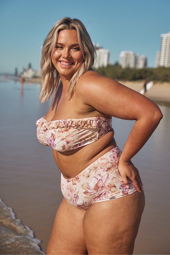 Blonde model posing in light pink floral strapless bikini on beach