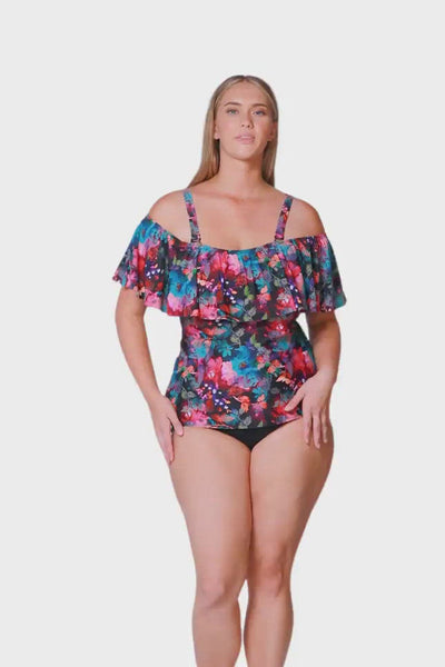blonde size 18 women wears a black based floral swimsuit that is worn off the shoulder with adjustable and removable strap options