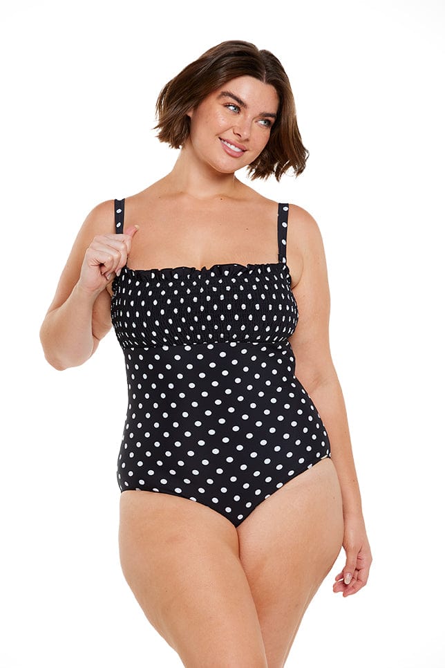 Brunette model wears flattering shirred bandeau one piece in black and white dots