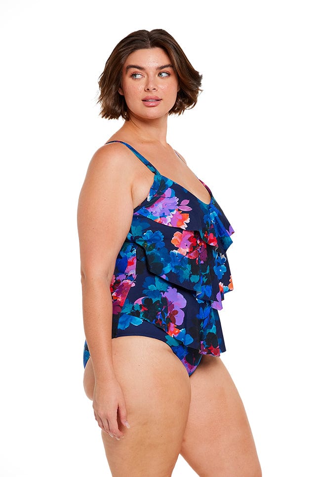 Brunette model wears colourful ruffle one piece swimsuit with adjustable straps