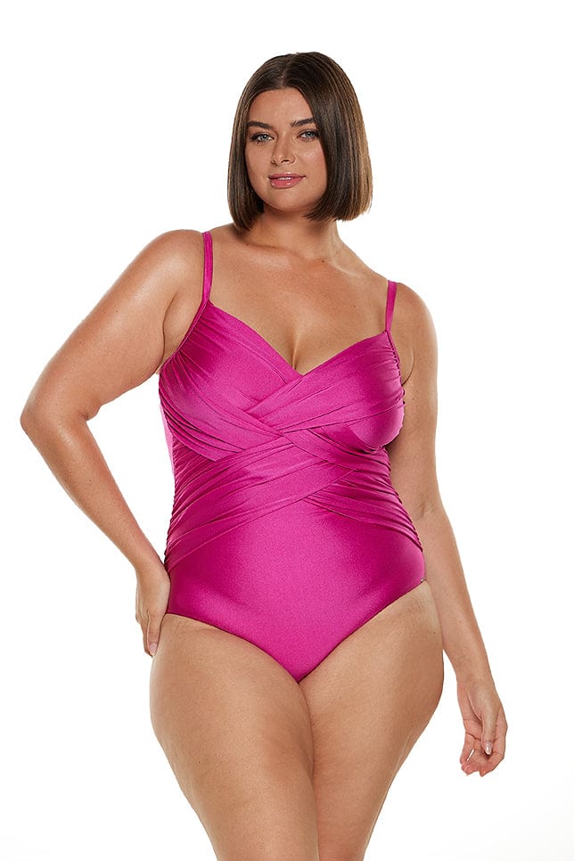 Brunette model wears hot pink one piece with criss crossing tummy control front and adjustable straps