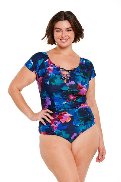 Brunette model wears navy blue floral full coverage one piece with tie front and cap sleeves
