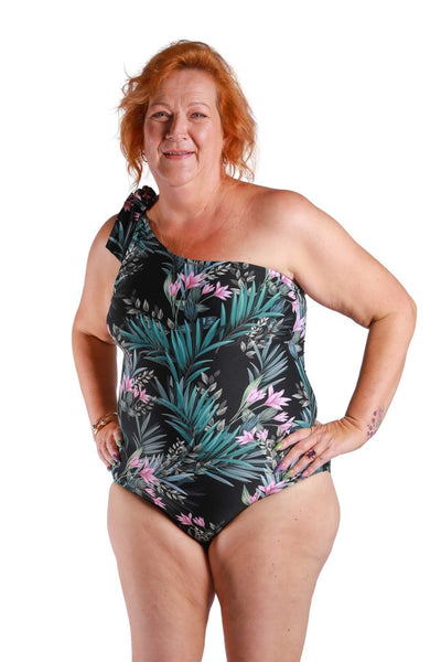 red haired post mastectomy women wearing black floral one shoulder swimsuit with tie on the shoulder