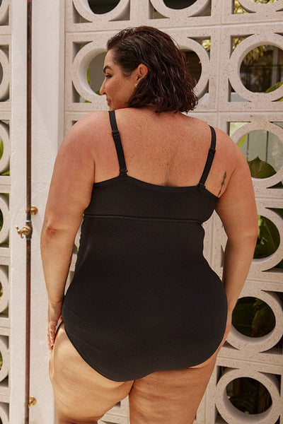 Brunette plus size model wears black one piece swimsuit with underwire support