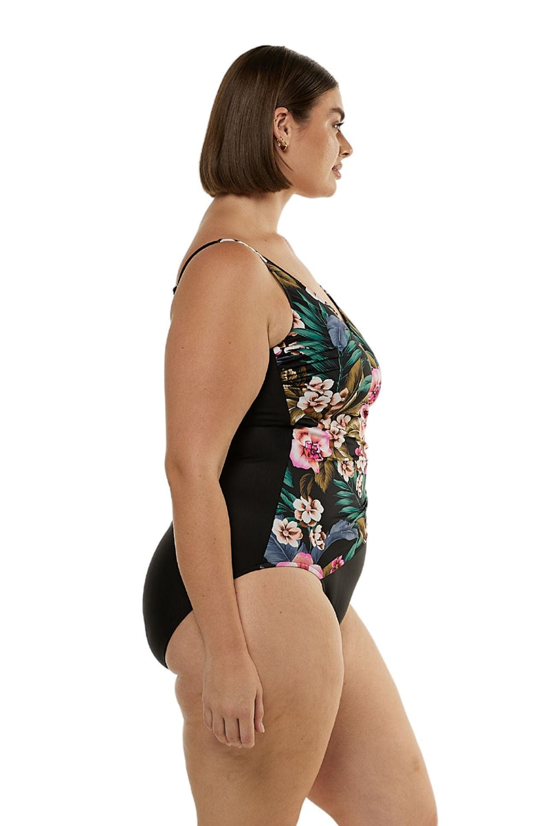Brunette model facing side wearing cross over tie one piece swimsuit curve