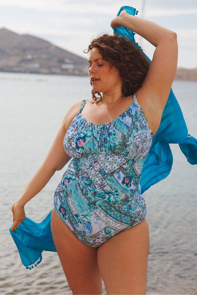 brunette model wearing underwire one piece in aqua blue tile print with turquoise sarong in her hands