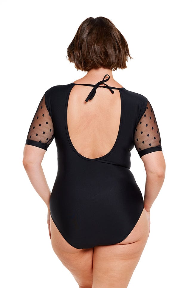 Brunette model wears black low back one piece with mesh sleeves and tie back detail
