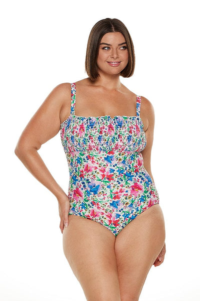 Brunette plus size model wearing shirred bandeau swimsuit with straps on in bright floral coloured print