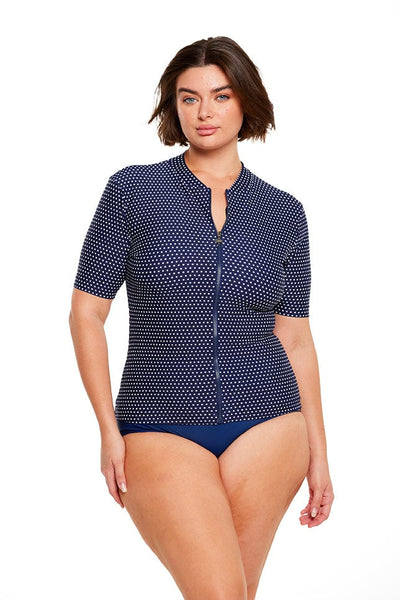 Brunette plus size model wears flattering navy and white dots short sleeve rash vest with front zip