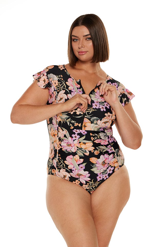 Brunette women wears figure flattering lilac and orange floral zip front one piece with stomach ruching and flutter sleeves