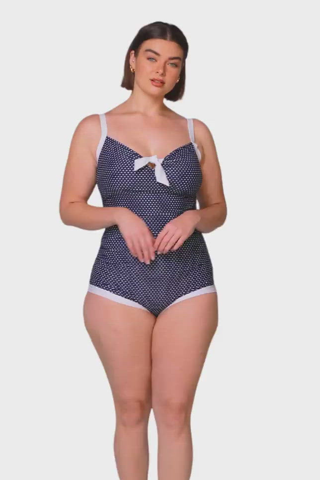brown haired model wearing retro navy and white dots one piece with a boyleg and bow detail