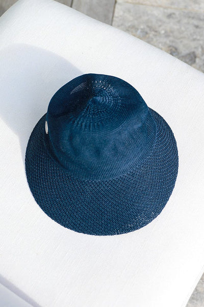 foldable navy blue straw beach hat laying on a white arm chair by the pool
