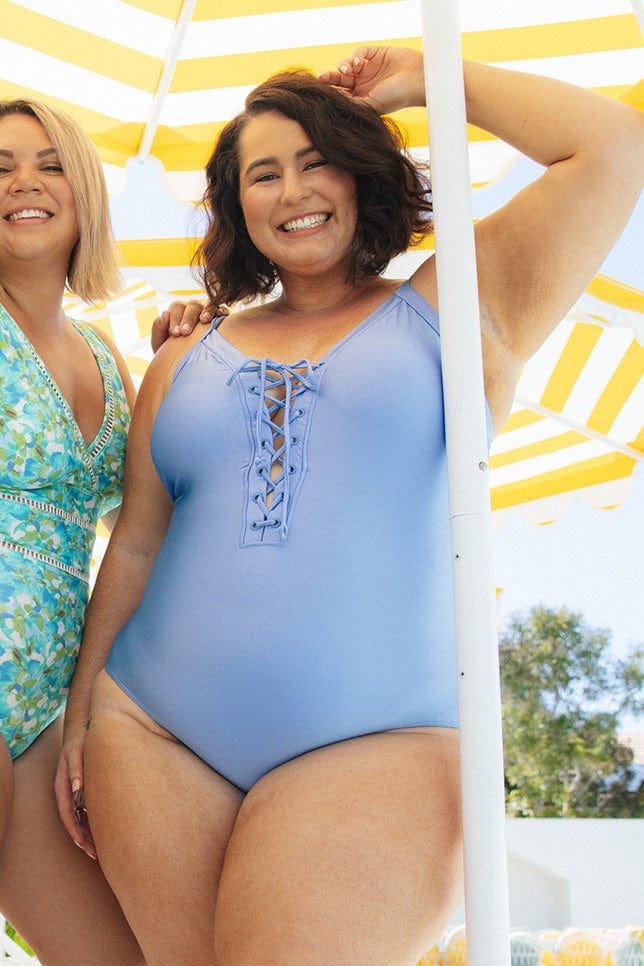 brunette model wearing lace up one piece in a light metallic blue