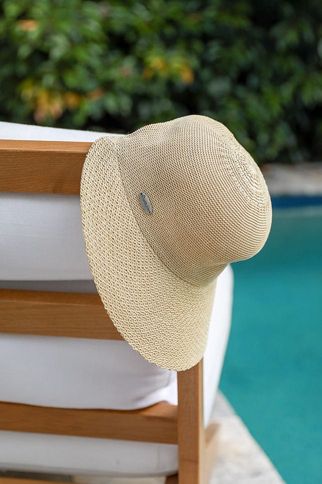 picture of natural coloured wide brim travel hat hanging off the side of a natural and white beach arm chair
