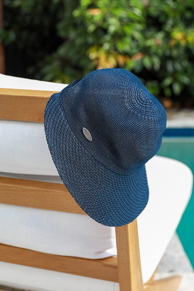 image of navy straw wide brim hat laying beside a pool on a natural and white beach chair