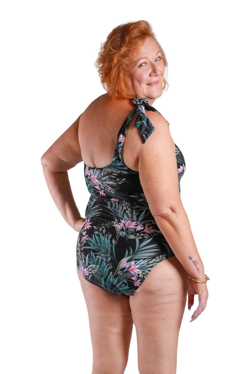 back of red haired model wearing one shoulder swimsuit in black and pink floral