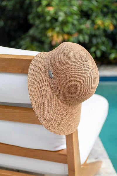 image of a wide brim camel brown travel hat hanging on the side of a beach chair positioned beside a blue polol