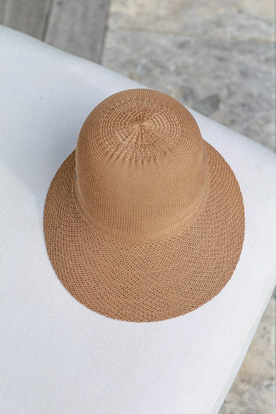 tan coloured straw beach hat laying on a white and natural coloured arm chair